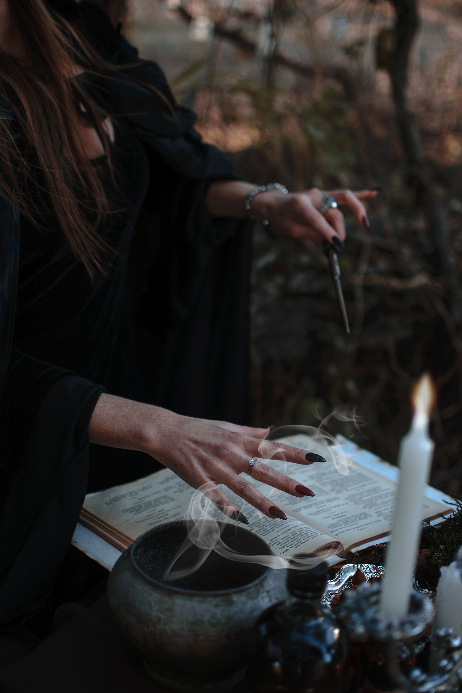 Ritual ao ar livre com livro, incenso, vela e vestes escuras