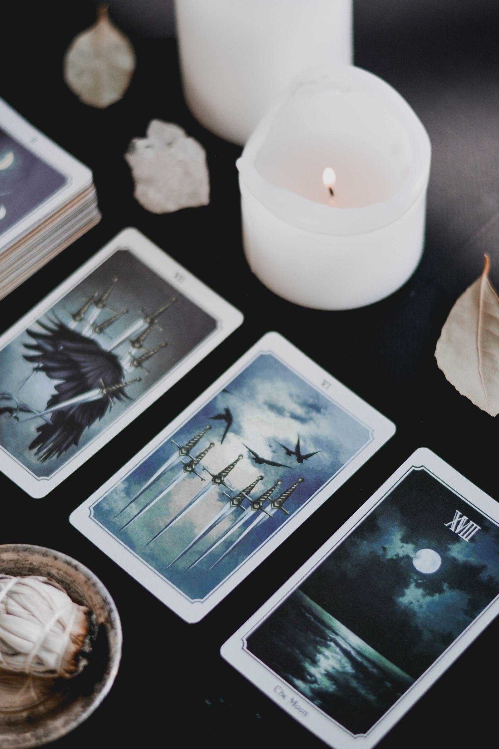 Cartas de tarot, vela acesa e ervas sobre uma superfície escura